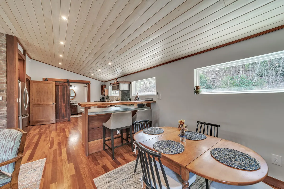 This image features a welcoming dining table set near a kitchen island, illuminated by large windows that invite in natural light. The setting is warm and communal, suggesting a space where guests gather to share meals and stories after a day out. The arrangement hints at the pleasures of enjoying local wine and preparing dinners together, connecting the inside experience to the exploration of local flavors.