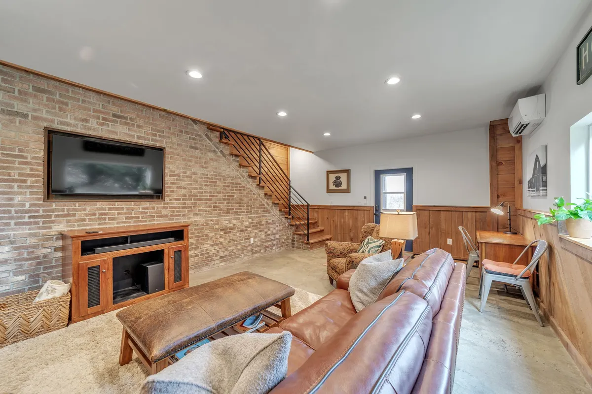 A welcoming living area centers around a leather sofa and coffee table, with a prominent brick wall and television creating a cozy nook. The arrangement is perfect for enjoying movie nights or sharing stories with family and friends, and the space is bathed in soft natural light, echoing the theme of comfort and togetherness.
