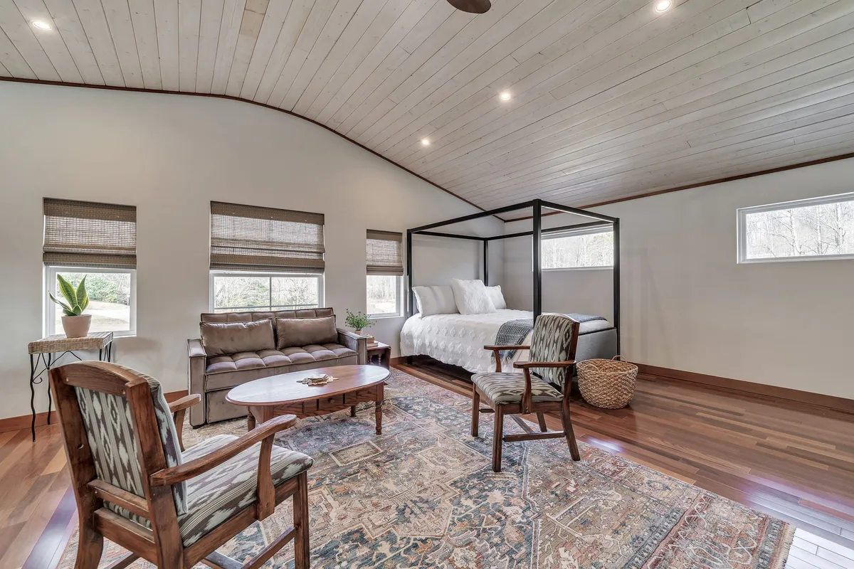 A spacious bedroom with a canopy bed, seating area, area rug, and large windows that allow natural light to pour in. The relaxed atmosphere is perfect for leisurely mornings or quiet evenings, with space for unpacking and enjoying private moments.